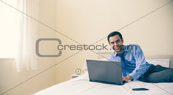 Content man lying on a bed using a laptop