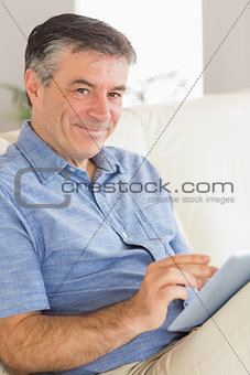 Smiling man sitting on a sofa using a tablet pc
