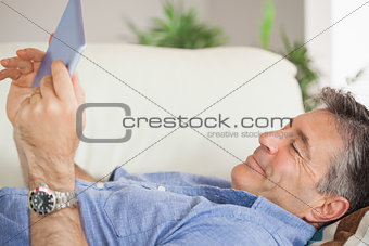 Smiling man laying on a sofa using a tablet pc