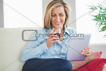 Smiling woman drinking wine and using a tablet pc