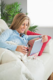 Smiling woman lying on a sofa drinking wine and using a tablet pc