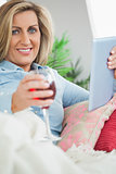 Smiling woman lying on a sofa drinking wine and using a tablet pc
