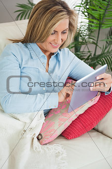 Smiling woman lying on a sofa using a tablet pc