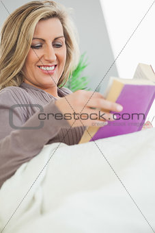 Smiling woman lying on sofa reading a book