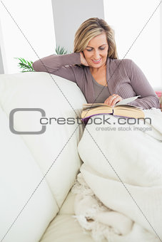 Smiling woman reading a book on a sofa