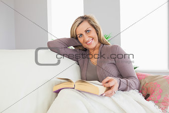 Smiling woman holding a book and lying on a sofa