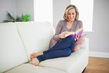 Smiling woman lying on a sofa reading a book