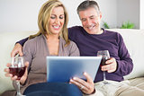 Happy couple watching their tablet pc and drinking wine