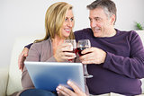 Happy couple toasting with wine sitting on a sofa