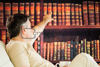 Sitting man picking a book in a reading room and drinkig coffee