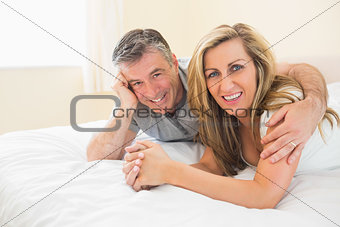 Happy couple lying on a bed looking at camera