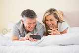 Happy couple lying on a bed and watching a mobile phone