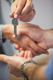 Estate agent giving house key to customer while shaking hands