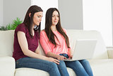 Two teenagers sitting on a sofa and watching a laptop