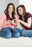 Two smiling girls sitting on a sofa looking at a mobile phone