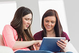 Two happy girls sitting on a sofa using a tablet pc