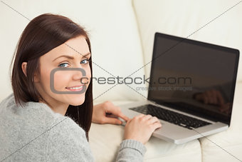 Smiling girl using a laptop on a sofa looking at camera