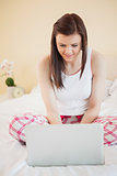 Smiling girl using a laptop sitting on her bed