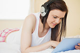 Smiling girl listening to music and using a tablet pc lying on a bed