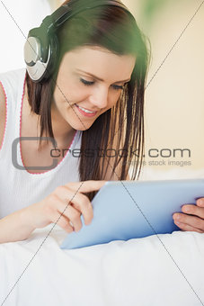 Happy girl listening to music and using a tablet pc lying on a bed