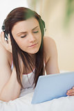 Relaxed girl listening to music and using a tablet pc lying on a bed