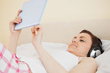 Smiling girl listening music and using a tablet pc lying on a bed