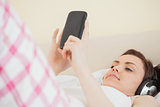 Smiling girl listening to music and using a mobile phone lying on a bed