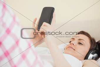 Smiling girl listening to music and using a mobile phone lying on a bed