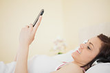 Smiling girl listening music on her smartphone lying on bed