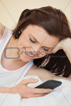 Cheerful girl using a mobile phone lying on a bed