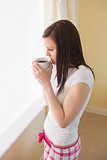 Girl drinking a cup of coffee standing in a bedroom
