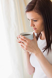 Thoughtful girl holding a cup of coffee and looking away