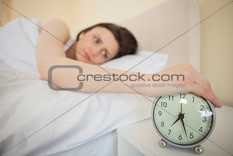 Tired girl turning off her alarm clock