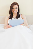 Smiling girl looking at camera using a tablet pc lying on a bed