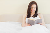Smiling girl reading a book lying on a bed
