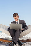 Businessman typing on his laptop in a hammock and smiling