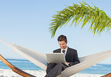 Smiling businessman using laptop and sitting in hammock