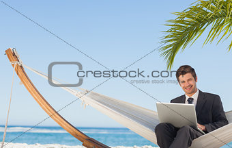 Businessman sitting in hammock using laptop looking at camera