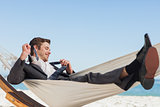 Smiling businessman lying in hamock taking off his tie