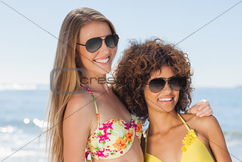 Two friends wearing sunglasses on the beach and smiling