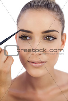 Smiling woman applying make up on her eyebrows