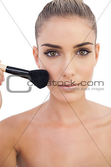 Serious woman applying powder on her cheeks