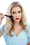 Serious blonde model in blue dress applying make up