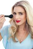 Amused blonde model in blue dress applying make up