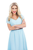 Smiling blonde model in blue dress posing crossed arms