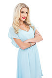 Pleased blonde model in blue dress posing crossed arms