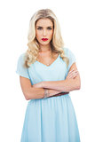 Severe blonde model in blue dress posing crossed arms