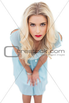 Serious blonde model in blue dress posing hands on the thighs