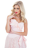 Contemplative blonde model in pink dress posing a finger on the mouth