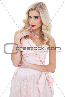Contemplative blonde model in pink dress posing a finger on the mouth